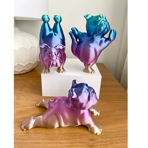 May include: Three 3D printed bulldog figurines in different poses. The figurines are painted in a gradient of blue, purple, and gold.