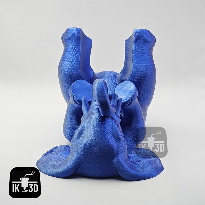 May include: A blue 3D printed elephant figurine lying on its back with its legs in the air. The elephant has a textured surface and is made of a smooth, glossy material.