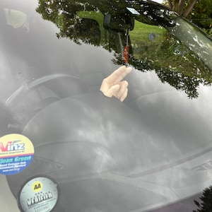 May include: A car windshield with a hand gesture sticker, a "Clean Green" sticker from "Vinz" and a "Verified" sticker from "AA".