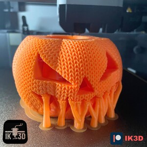 Pode incluir: Uma ab&oacute;bora laranja impressa em 3D com uma cara assustadora e detalhes pingando. A ab&oacute;bora est&aacute; sendo impressa em uma impressora 3D.