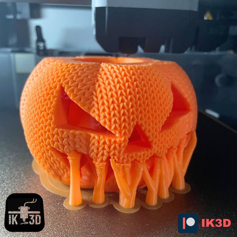 Pode incluir: Uma ab&oacute;bora laranja impressa em 3D com uma cara assustadora e detalhes pingando. A ab&oacute;bora est&aacute; sendo impressa em uma impressora 3D.