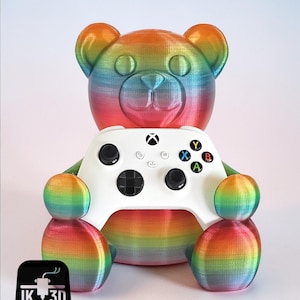 Könnte beinhalten: Ein mehrfarbiger Teddybär-Controllerhalter, der einen weißen Xbox-Controller hält. Der Bär ist mit einem Regenbogen-Farbverlauf gestaltet, der Rot, Orange, Gelb, Grün, Blau und Lila umfasst. Der Halter hat ein 3D-gedrucktes Aussehen.