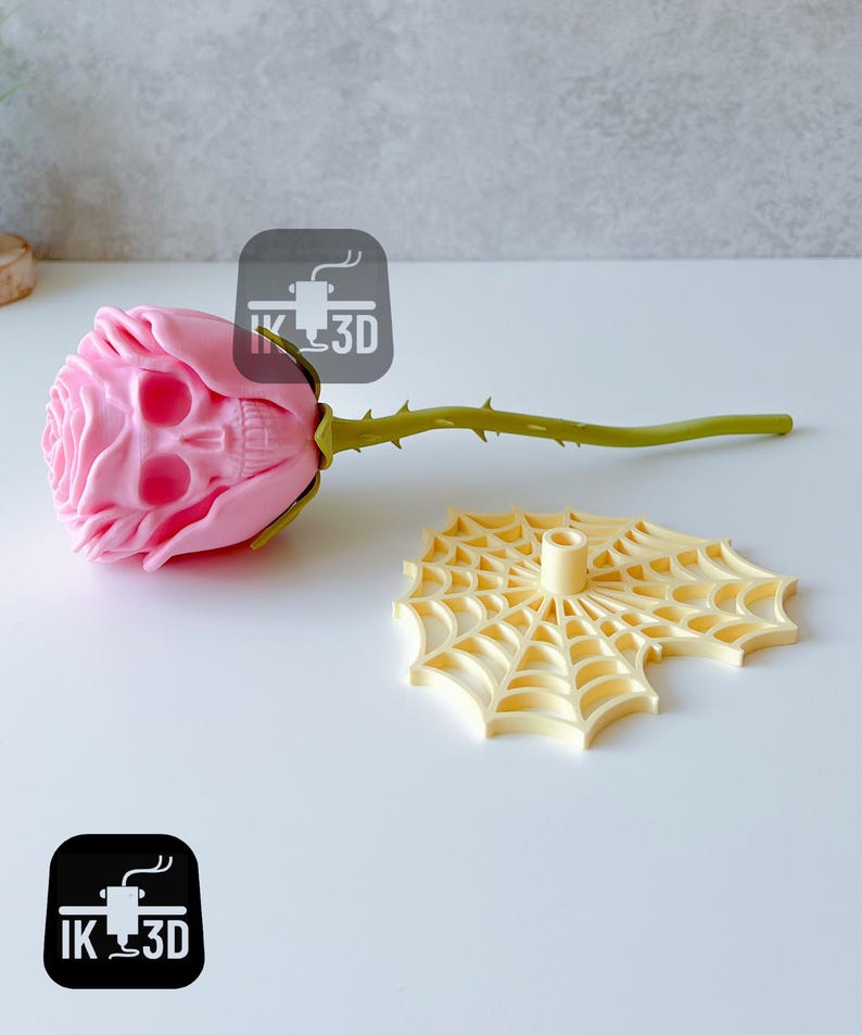 Puede incluir: Una rosa rosa con una flor en forma de calavera y un tallo verde con espinas. Junto a ella, un soporte amarillo con forma de telara&ntilde;a. La rosa es un art&iacute;culo decorativo &uacute;nico.