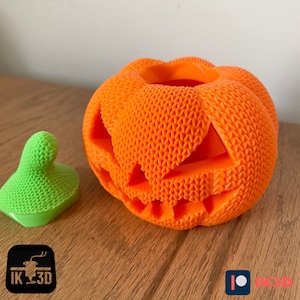 Pode incluir: Uma ab&oacute;bora laranja impressa em 3D com um rosto de ab&oacute;bora esculpido. A ab&oacute;bora tem uma superf&iacute;cie texturizada e est&aacute; sentada em uma superf&iacute;cie de madeira.