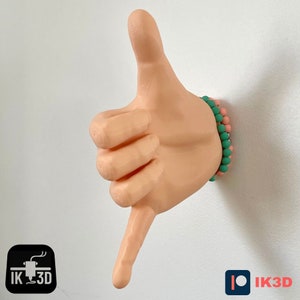 May include: A 3D printed hand sculpture in a light skin tone, making the shaka sign, with a pink and green beaded bracelet on the wrist.