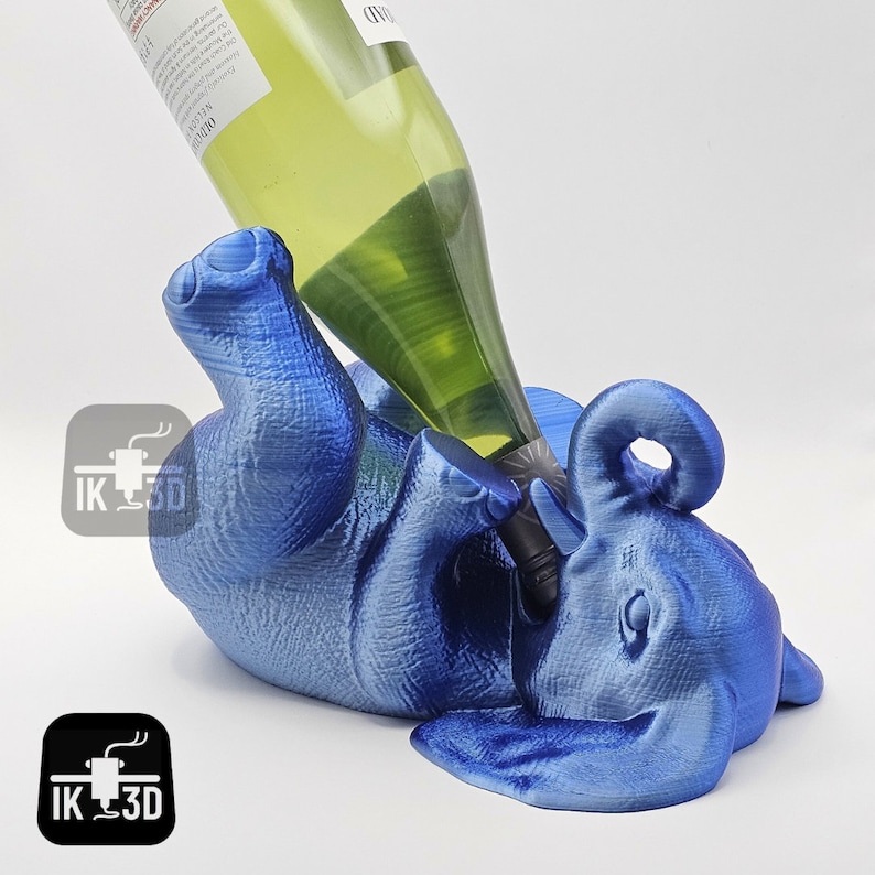 May include: A blue elephant shaped wine bottle holder. The elephant is lying on its side with its trunk raised. A bottle of wine is being poured into the elephant's trunk.