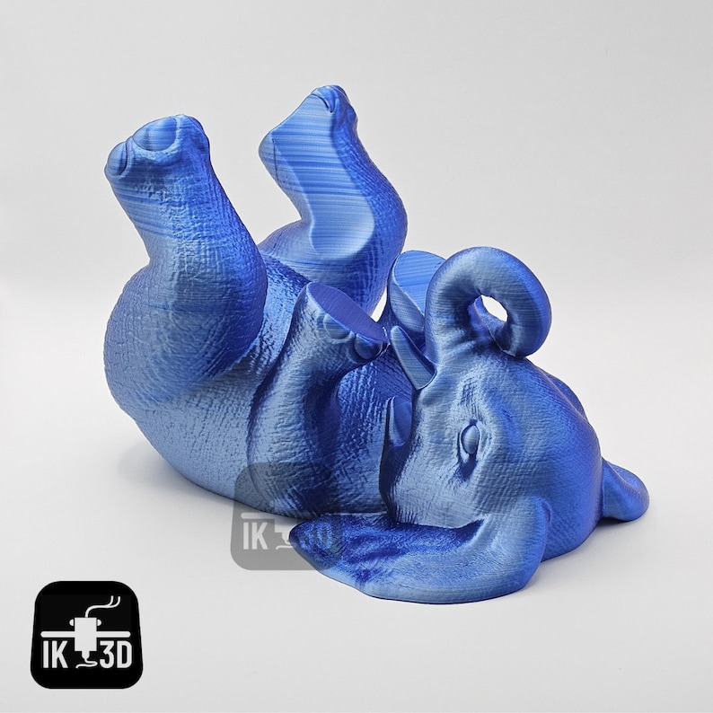 May include: A blue 3D printed elephant figurine lying on its back with its legs in the air. The elephant has a textured surface and a curled trunk.