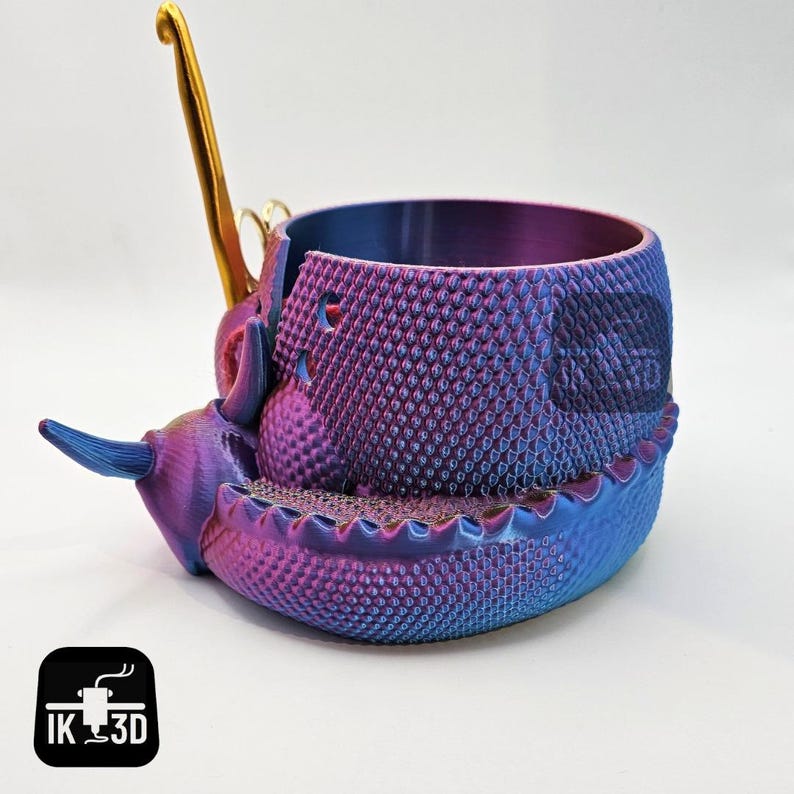 May include: A purple and blue iridescent 3D printed dragon-shaped yarn bowl with a gold metal hook.