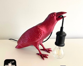 May include: A red crow-shaped lamp with a black cord and a black light bulb. The lamp is made of 3D printed plastic.
