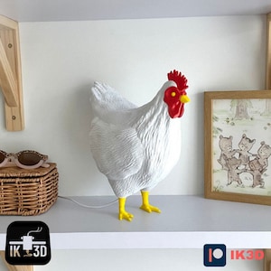 May include: White ceramic chicken figurine with red comb and yellow feet. The chicken is standing on a white shelf with a wooden frame behind it.