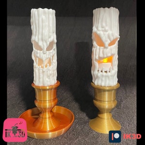 Puede incluir: Dos velas blancas de Halloween con caras de miedo. Las velas est&aacute;n en candelabros dorados con una base redonda.