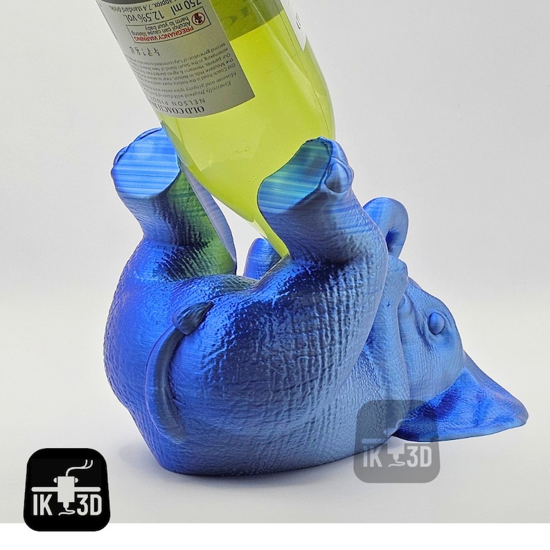 May include: A blue 3D printed elephant bottle holder with a wine bottle in its mouth. The bottle is labeled "OLD COACH NELSONIC (Alcohol) PREGNANCY WARNING 250 ml 12.5% vol."