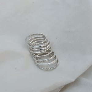 Puede incluir: Un conjunto de ocho anillos apilables de plata con diferentes texturas, incluyendo un diseño trenzado, martillado y estriado.