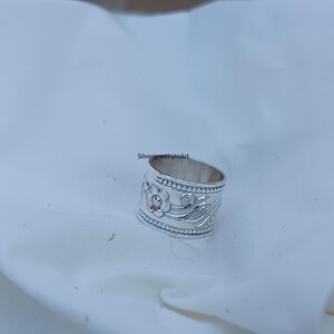 Op de afbeelding: Een zilveren ring met een bloemenmotief. De ring is breed en heeft een getextureerde band.