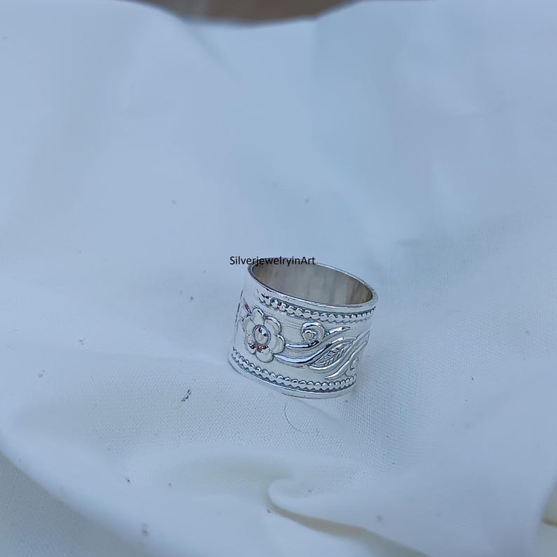 Op de afbeelding: Een zilveren ring met een bloemenmotief. De ring is breed en heeft een getextureerde band.