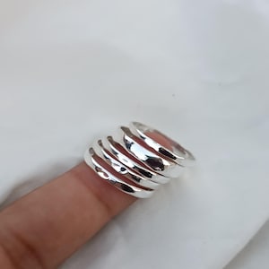 Może przedstawiać: Zestaw pięciu srebrnych pierścionków do nakładania na siebie. Pierścionki są gładkie i mają fakturę młotkową. Są ułożone na palcu.