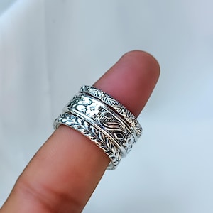 Peut inclure: Une bague en argent orn&eacute;e de motifs floraux et de feuilles complexes. La bague est compos&eacute;e de plusieurs anneaux, chacun avec un design unique. La bague est port&eacute;e sur un doigt, mettant en valeur le savoir-faire d&eacute;taill&eacute; et la surface brillante du m&eacute;tal.