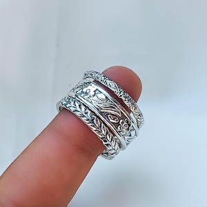 Peut inclure: Anneaux en argent avec des motifs floraux et de feuilles complexes. Les anneaux sont empil&eacute;s sur un doigt, mettant en valeur les motifs d&eacute;taill&eacute;s. Les anneaux ont une esth&eacute;tique vintage ou boh&egrave;me.