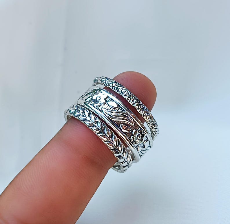 Peut inclure: Anneaux en argent avec des motifs floraux et de feuilles complexes. Les anneaux sont empil&eacute;s sur un doigt, mettant en valeur les motifs d&eacute;taill&eacute;s. Les anneaux ont une esth&eacute;tique vintage ou boh&egrave;me.