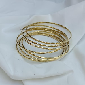May include: Set of six gold-toned hammered metal bangles. The bangles are stacked on top of each other, creating a layered look.