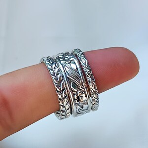 Peut inclure: Gros plan sur quatre bagues en argent orn&eacute;es de motifs floraux et de feuilles complexes. Les bagues sont empil&eacute;es sur un doigt, mettant en valeur les motifs d&eacute;taill&eacute;s. Les bagues ont une esth&eacute;tique vintage ou boh&egrave;me.