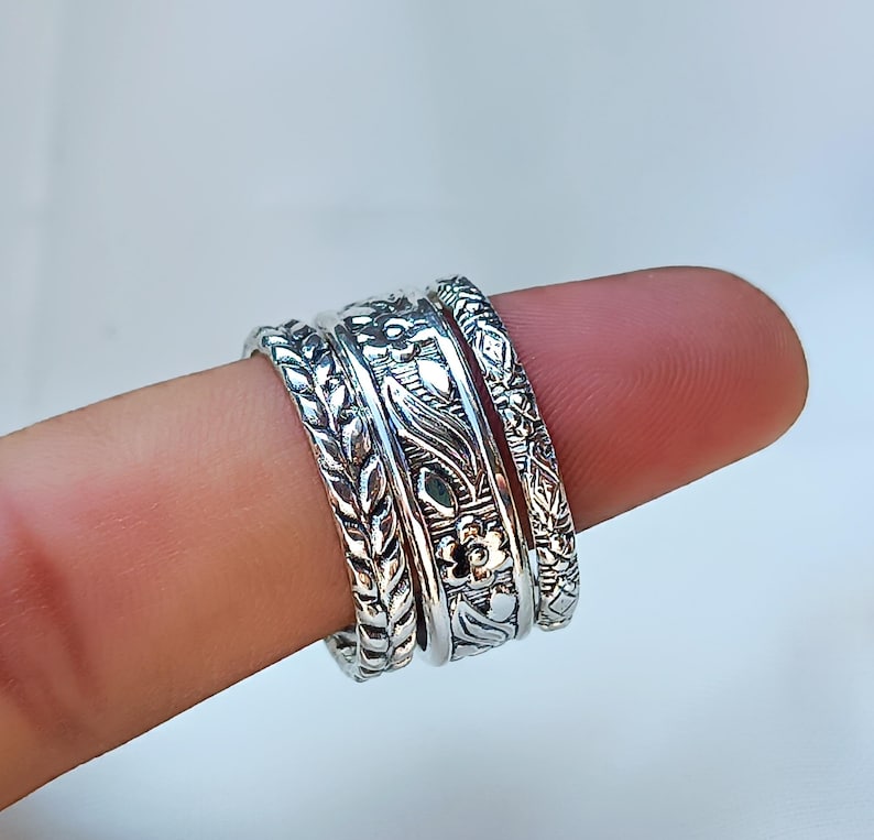 Peut inclure: Gros plan sur quatre bagues en argent orn&eacute;es de motifs floraux et de feuilles complexes. Les bagues sont empil&eacute;es sur un doigt, mettant en valeur les motifs d&eacute;taill&eacute;s. Les bagues ont une esth&eacute;tique vintage ou boh&egrave;me.