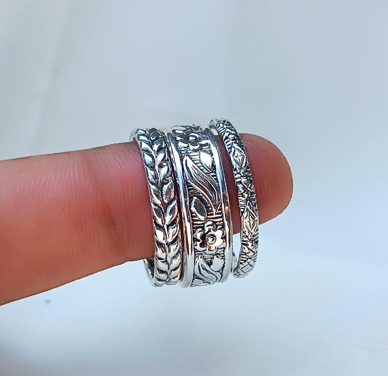 Peut inclure: Gros plan sur quatre bagues en argent orn&eacute;es de motifs floraux et de feuilles d&eacute;taill&eacute;s. Les bagues sont empil&eacute;es sur un doigt, mettant en valeur les motifs complexes. Chaque bague pr&eacute;sente une texture unique.