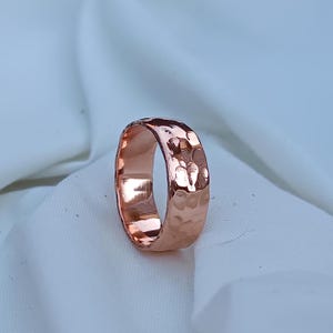 Peut inclure: Une bague en cuivre martelé avec une bande large. La bague a une surface texturée et une couleur brun rougeâtre chaud.