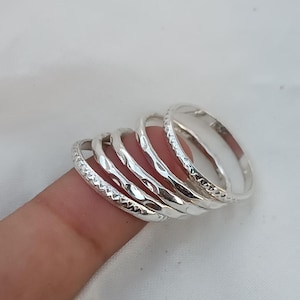 Puede incluir: Conjunto de cinco anillos apilables de plata con diferentes texturas. Los anillos se llevan en un dedo.