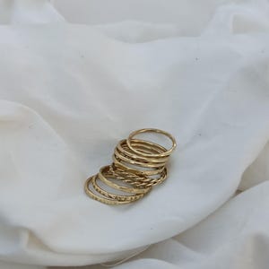 Könnte beinhalten: Ein Satz von neun goldfarbenen Stapelringen mit verschiedenen Texturen. Die Ringe sind übereinander gestapelt und erzeugen einen geschichteten Look.