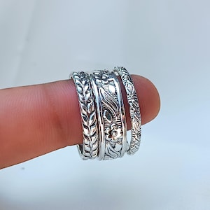 Peut inclure: Gros plan sur quatre bagues en argent orn&eacute;es de motifs floraux et de feuilles d&eacute;taill&eacute;s. Les bagues sont empil&eacute;es sur un doigt, mettant en valeur les motifs complexes. Chaque bague pr&eacute;sente une texture unique.