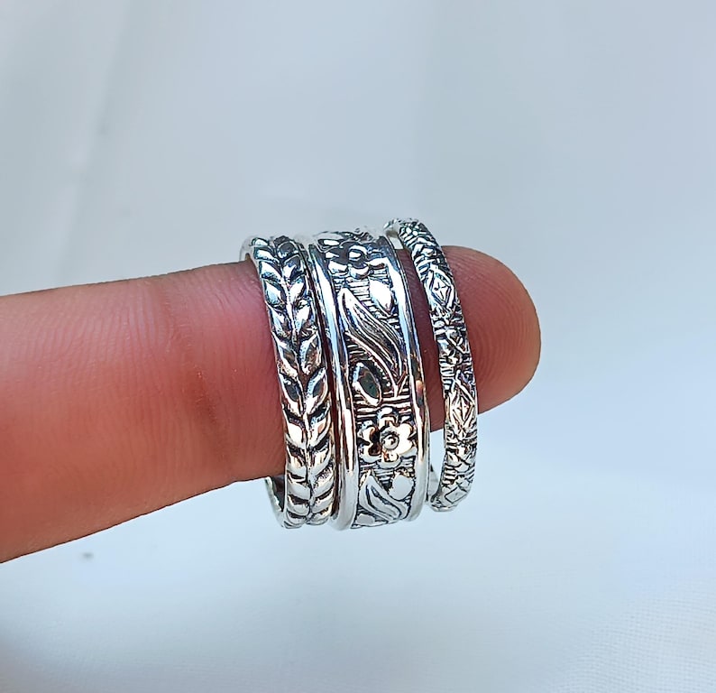 Peut inclure: Gros plan sur quatre bagues en argent orn&eacute;es de motifs floraux et de feuilles d&eacute;taill&eacute;s. Les bagues sont empil&eacute;es sur un doigt, mettant en valeur les motifs complexes. Chaque bague pr&eacute;sente une texture unique.
