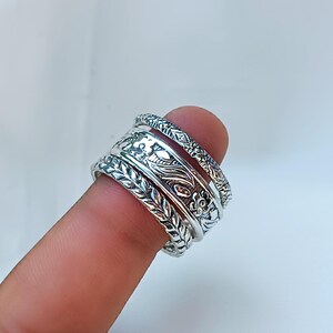 Peut inclure: Anneaux en argent avec des motifs floraux et de feuilles complexes. Les anneaux sont empil&eacute;s sur un doigt, mettant en valeur les motifs d&eacute;taill&eacute;s. Les anneaux ont une esth&eacute;tique vintage ou boh&egrave;me.