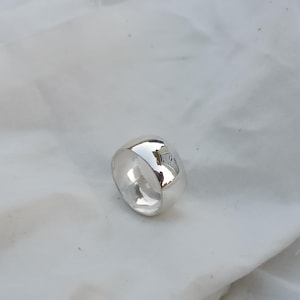 Peut inclure: Une bague en argent avec une surface arrondie et lisse. La bague est épaisse et a une finition polie.