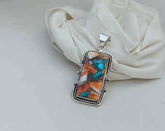 May include: A silver pendant with a rectangular turquoise and orange stone set in a silver bezel. The pendant has a silver bail for attaching to a chain.