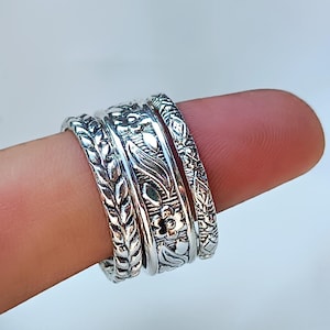 Peut inclure: Quatre bagues en argent orn&eacute;es de motifs floraux et de feuilles d&eacute;taill&eacute;s. Les bagues sont empil&eacute;es sur un doigt, mettant en valeur les motifs complexes. Les bagues ont une esth&eacute;tique vintage ou boh&egrave;me.