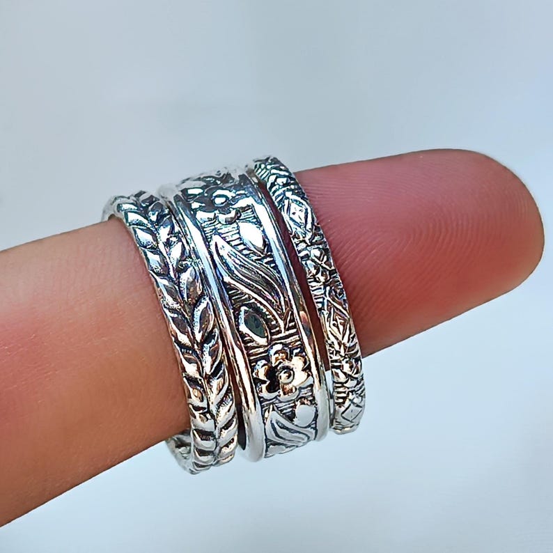 Peut inclure: Quatre bagues en argent orn&eacute;es de motifs floraux et de feuilles d&eacute;taill&eacute;s. Les bagues sont empil&eacute;es sur un doigt, mettant en valeur les motifs complexes. Les bagues ont une esth&eacute;tique vintage ou boh&egrave;me.
