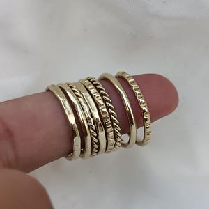 Könnte beinhalten: Ein Set aus sieben goldfarbenen Stapelringen mit verschiedenen Texturen, darunter gehämmert, Seil und strukturiert.