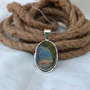 May include: An oval-shaped pendant with a green and brown tiger's eye stone set in a silver frame.