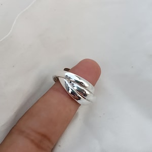 May include: A silver ring with a unique, interwoven design. The ring is made of three bands that are twisted together to create a smooth, continuous surface.