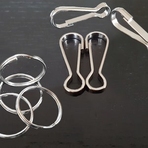 Può includere: Un set di portachiavi e moschettoni argentati. I portachiavi sono impilati uno sopra l'altro. I moschettoni sono separati.