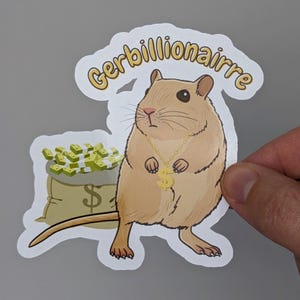 Puede incluir: Una pegatina troquelada que muestra un jerbo de color tostado con una cadena dorada y un colgante de signo de dólar. Detrás del jerbo hay un saco de color tostado lleno de fajos de billetes verdes. El texto Gerbillionaire aparece en amarillo.