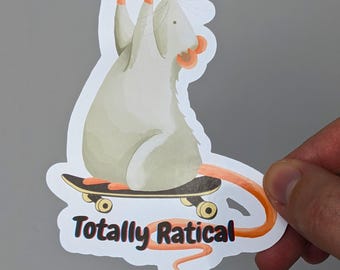 May include: A die-cut sticker featuring a light gray rat with orange ears and tail, standing on a black skateboard. The rat has its front paws raised in the air. Below the skateboard, the text Totally Ratical is printed in black letters.