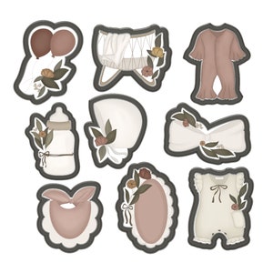 May include: A set of nine cookie cutters in the shape of baby-related items, including a crib, a bottle, a bib, a bow, a hat, and two onesies. The cutters are made of metal and have a brown finish.