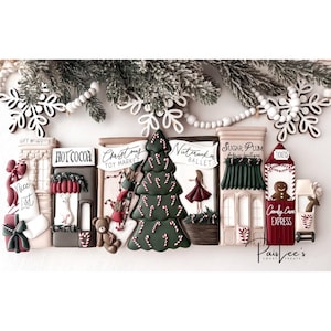 May include: A festive Christmas-themed display featuring gingerbread house-shaped cookies. The cookies are decorated with various holiday elements, including a Christmas tree, candy canes, and a ballerina. The color palette includes red, green, and white.