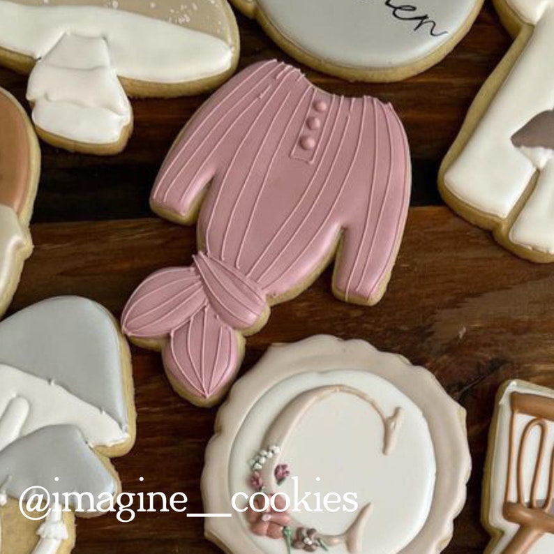 Puede incluir: Una colecci&oacute;n de galletas de az&uacute;car decoradas, que incluyen una galleta de su&eacute;ter rosa, una galleta de sombrero gris, una galleta con la letra C y acentos florales, y una galleta con el texto "@imagine_cookies".