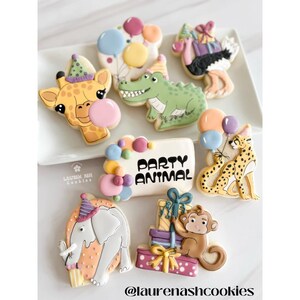 K&ouml;nnte beinhalten: Ein Set aus neun dekorierten Zuckerkeksen mit Tierfiguren, Ballons und dem Text "Party Animal". Die Kekse sind mit buntem Zuckerguss und Streuseln verziert.