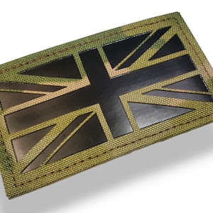 Peut inclure: Un patch de drapeau Union Jack noir sur un fond de tissu camouflage vert. Le patch est cousu avec un fil brun.