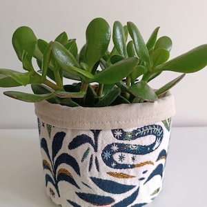 Peut inclure: Un plant de jade dans un pot en tissu blanc avec un motif de serpent bleu et or et de fleurs.
