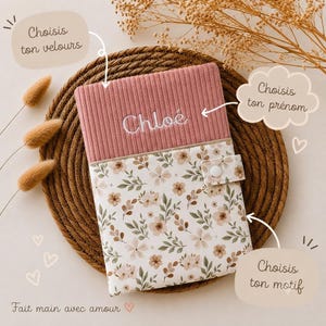 Peut inclure: Une couverture de carnet rectangulaire en tissu composée d'une partie supérieure en velours côtelé rose poudré brodée du prénom Chloé en blanc et d'une partie inférieure à motif floral, fermée par une patte à bouton-pression blanc.